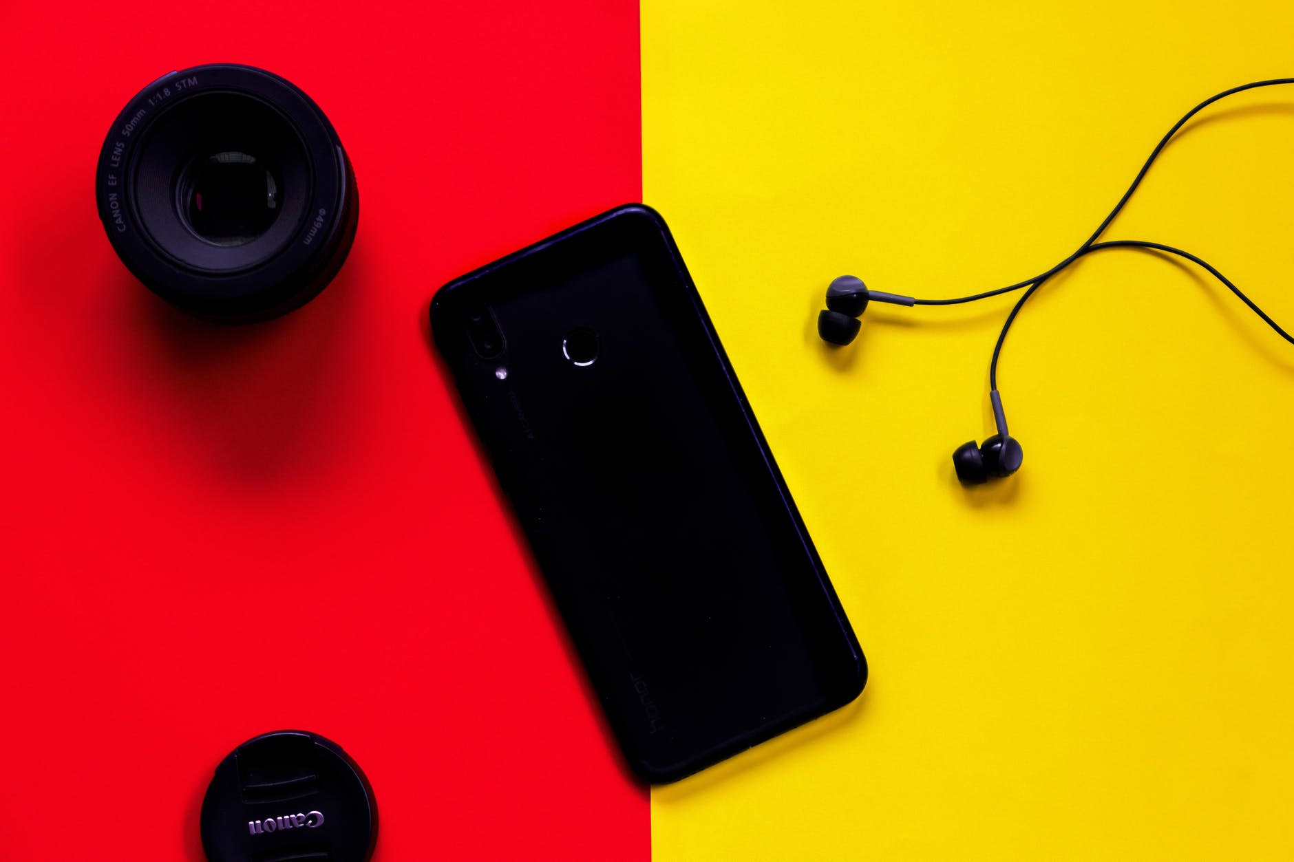 black smartphone besides earphones and camera lens